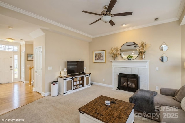 living area featuring baseboards, a tiled fireplace, light colored carpet, ceiling fan, and ornamental molding