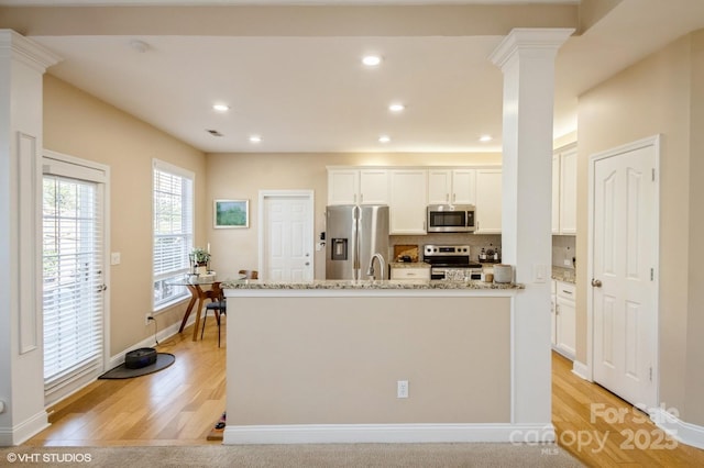 kitchen featuring appliances with stainless steel finishes, light wood-style floors, decorative columns, and tasteful backsplash