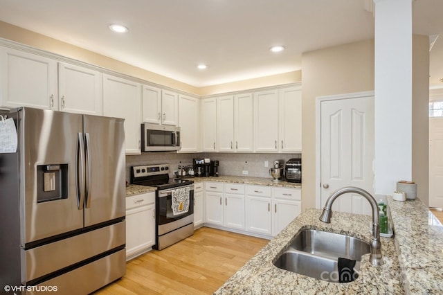 kitchen with a sink, white cabinetry, light wood-style floors, appliances with stainless steel finishes, and decorative backsplash