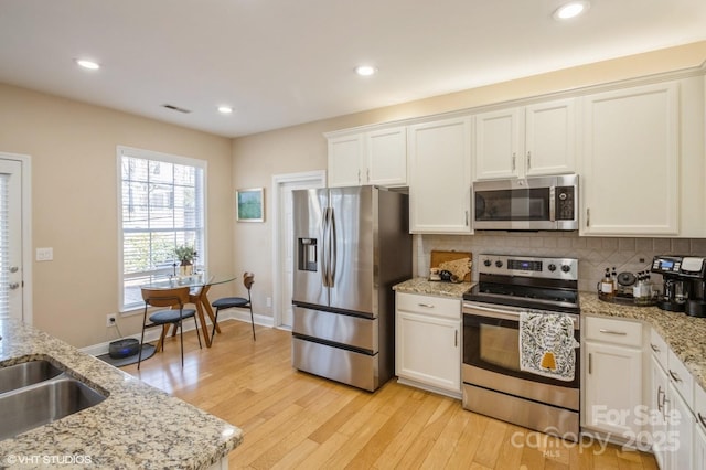 kitchen featuring light wood-style flooring, stainless steel appliances, visible vents, white cabinetry, and decorative backsplash