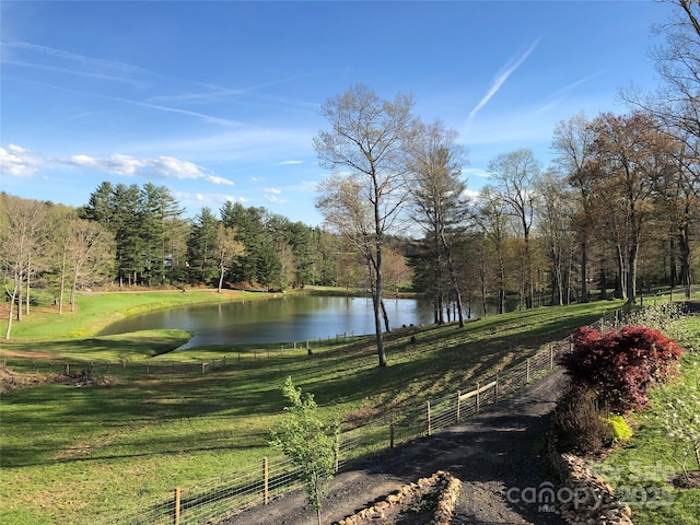 view of property's community featuring a water view, a forest view, fence, and a yard