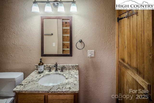 bathroom featuring a textured wall, vanity, and toilet