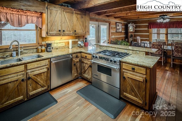 kitchen featuring stainless steel appliances, light wood-style flooring, a sink, beamed ceiling, and a peninsula