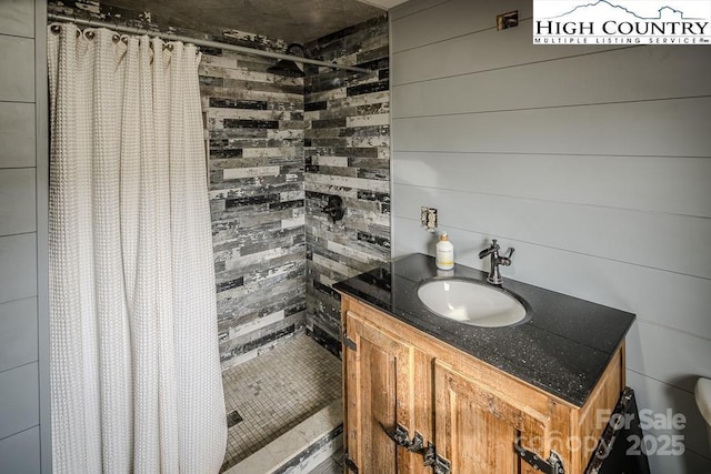 bathroom featuring tiled shower, wood walls, and vanity