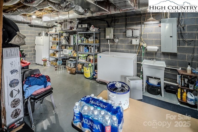 unfinished basement featuring white fridge, concrete block wall, freestanding refrigerator, and electric panel