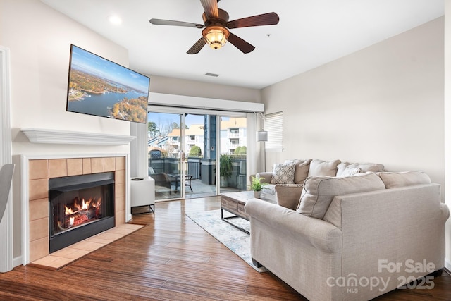 living room featuring a ceiling fan, a fireplace, visible vents, and wood finished floors