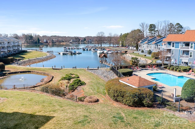 community pool with a dock, a water view, a yard, and fence