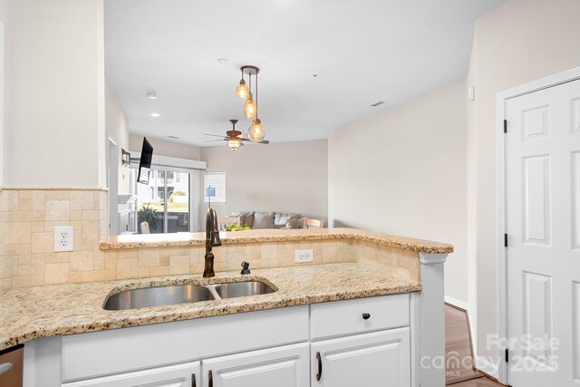 kitchen featuring pendant lighting, backsplash, white cabinetry, a sink, and light stone countertops