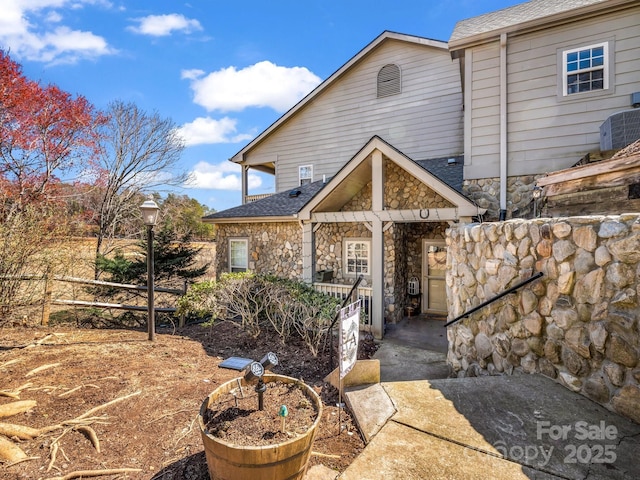 view of front of house with stone siding, a shingled roof, and fence