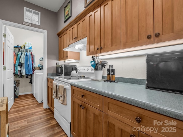 kitchen featuring light wood finished floors, electric stove, under cabinet range hood, stainless steel microwave, and brown cabinets