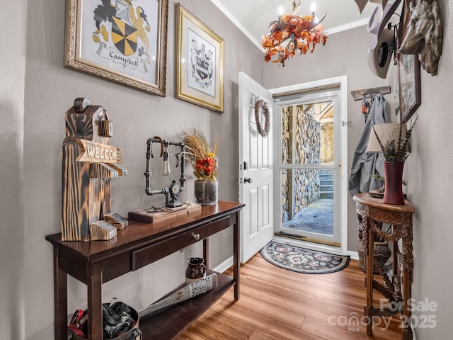 entrance foyer with baseboards, wood finished floors, an inviting chandelier, and ornamental molding