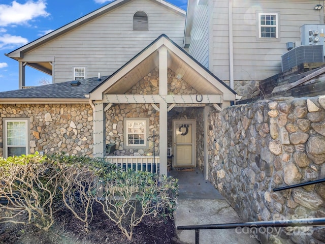 property entrance with stone siding, roof with shingles, and a porch