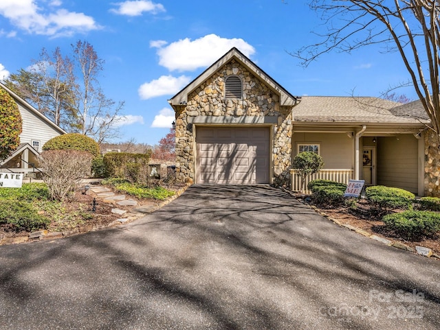 view of front facade with aphalt driveway, stone siding, a garage, and roof with shingles