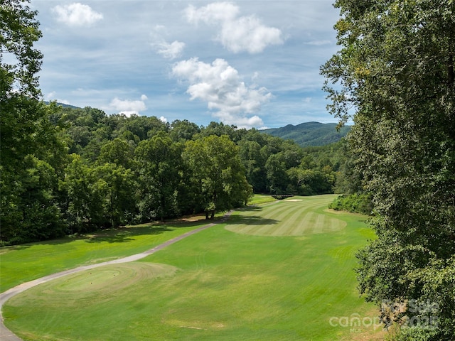 view of property's community with a mountain view, a view of trees, a lawn, and golf course view