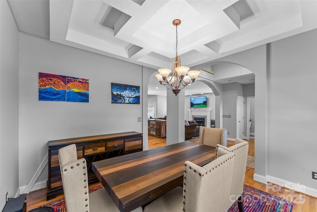 dining room with light wood finished floors, baseboards, a fireplace, arched walkways, and a notable chandelier