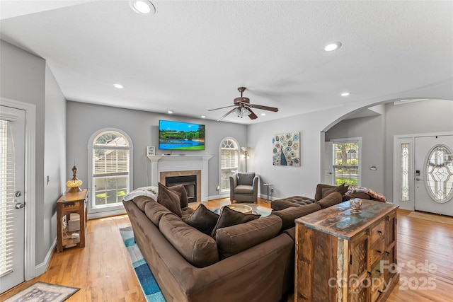 living area featuring recessed lighting, arched walkways, a glass covered fireplace, and light wood-style flooring