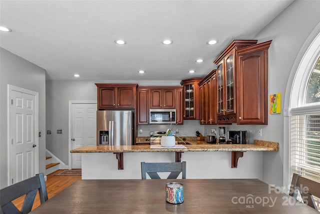 kitchen with a breakfast bar area, a peninsula, stainless steel appliances, and glass insert cabinets