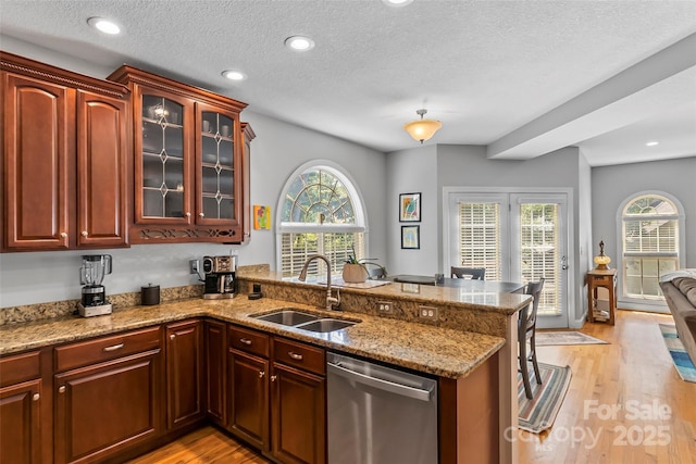 kitchen with a sink, stainless steel dishwasher, a peninsula, and light wood finished floors