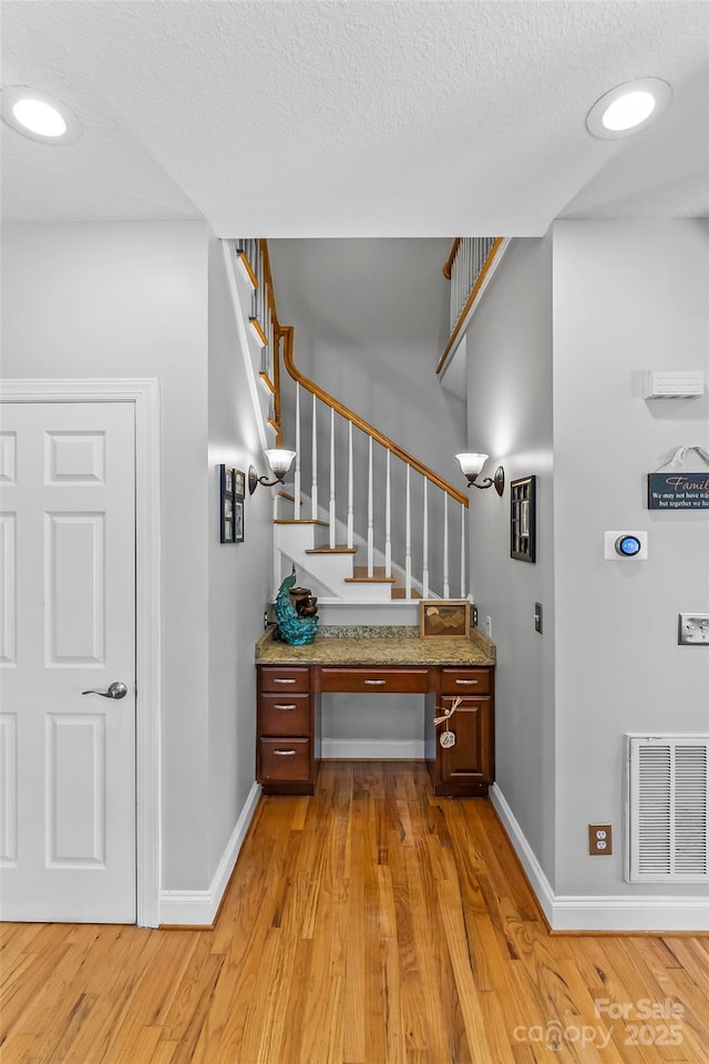 staircase with visible vents, a textured ceiling, baseboards, and wood finished floors