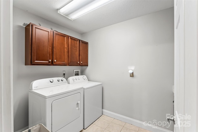 washroom with baseboards, washing machine and dryer, light tile patterned floors, cabinet space, and a textured ceiling