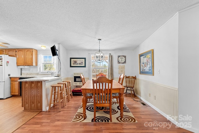 dining space featuring light wood-type flooring, visible vents, a wainscoted wall, heating unit, and a textured ceiling