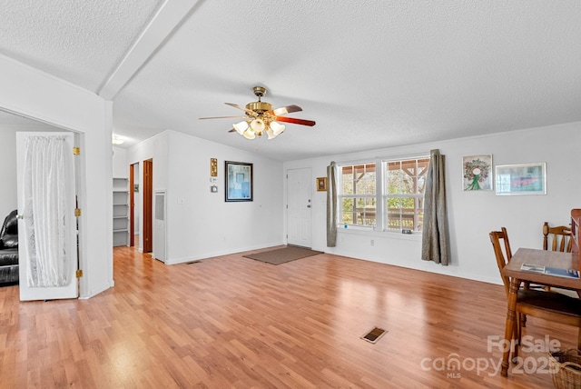 living room with light wood finished floors, visible vents, a textured ceiling, and lofted ceiling