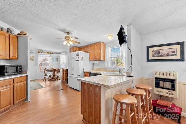 kitchen with stainless steel microwave, a peninsula, freestanding refrigerator, heating unit, and a sink