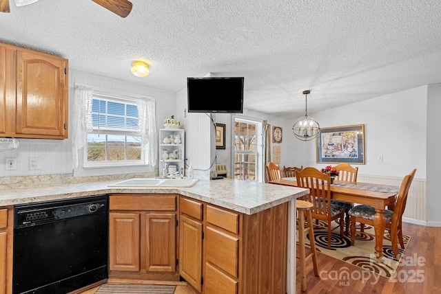 kitchen featuring a peninsula, a sink, light countertops, black dishwasher, and light wood-style floors