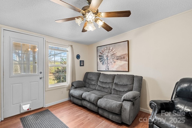 living area featuring a ceiling fan, baseboards, light wood-type flooring, and a textured ceiling