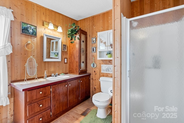 full bathroom with toilet, a stall shower, a textured ceiling, wood finished floors, and vanity