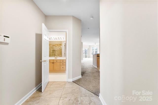 hallway featuring light tile patterned floors, baseboards, a sink, and light colored carpet