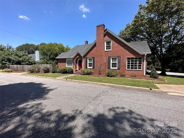 view of front of property featuring a front yard, brick siding, fence, and a chimney