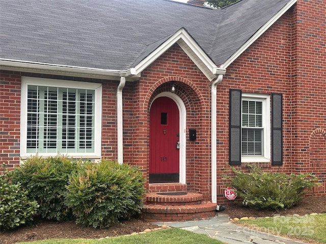 property entrance with a shingled roof and brick siding