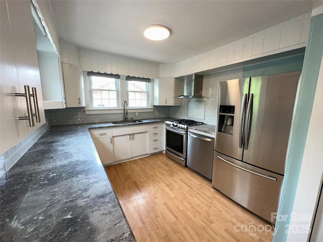 kitchen featuring dark countertops, appliances with stainless steel finishes, a sink, wall chimney range hood, and backsplash