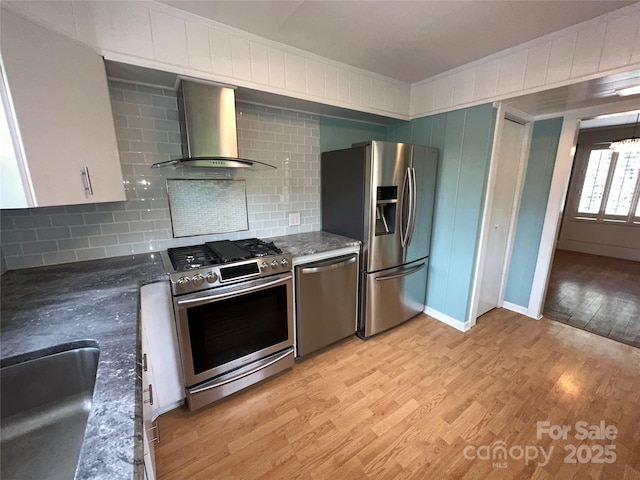 kitchen with stainless steel appliances, backsplash, light wood-style flooring, a sink, and wall chimney exhaust hood