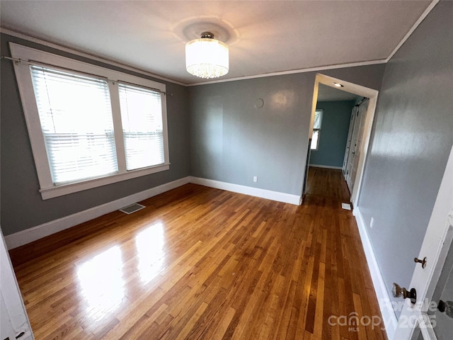 empty room with baseboards, visible vents, wood finished floors, and ornamental molding