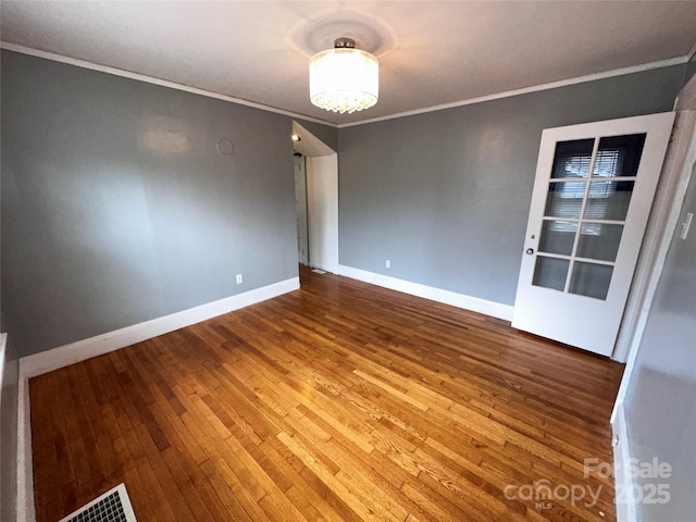 empty room featuring a notable chandelier, visible vents, baseboards, wood-type flooring, and crown molding