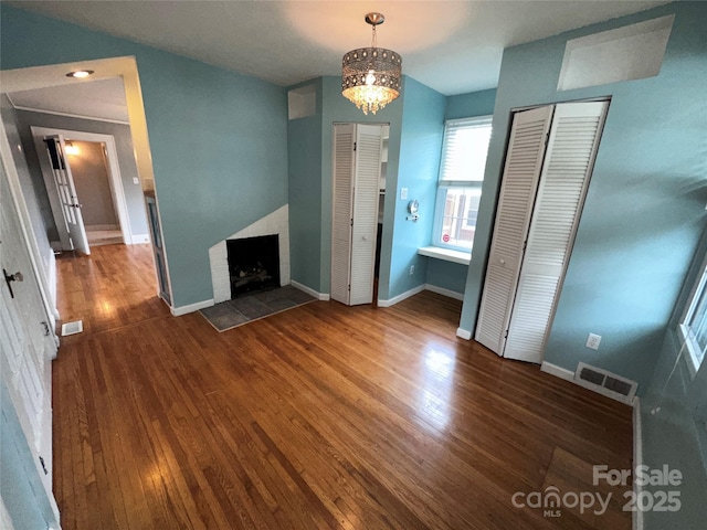 unfurnished living room featuring baseboards, visible vents, a fireplace with raised hearth, and wood finished floors