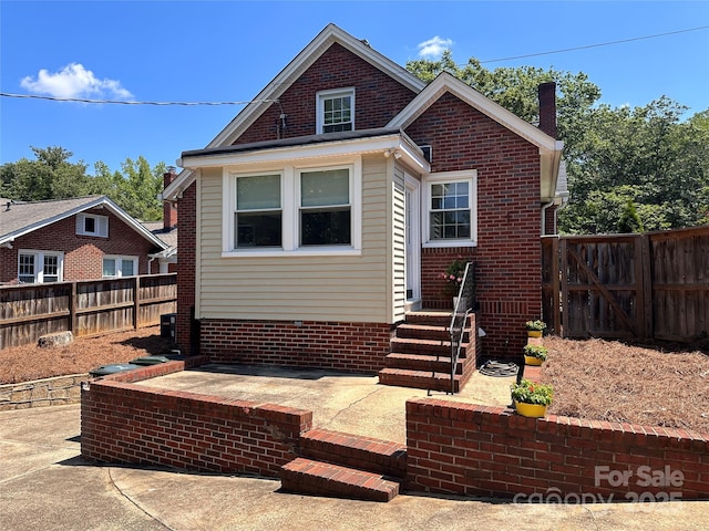 back of house featuring brick siding, fence, and a chimney