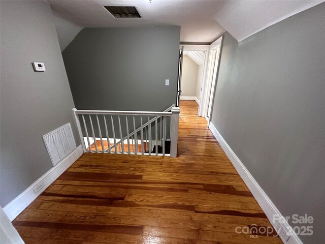 hall featuring baseboards, visible vents, wood finished floors, and an upstairs landing