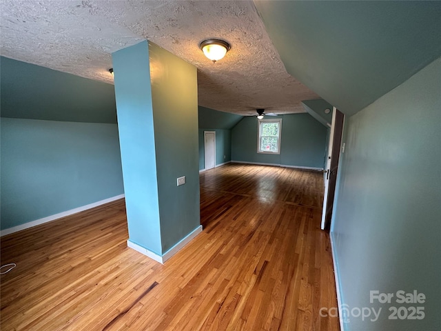 bonus room with a textured ceiling, wood finished floors, a ceiling fan, baseboards, and vaulted ceiling