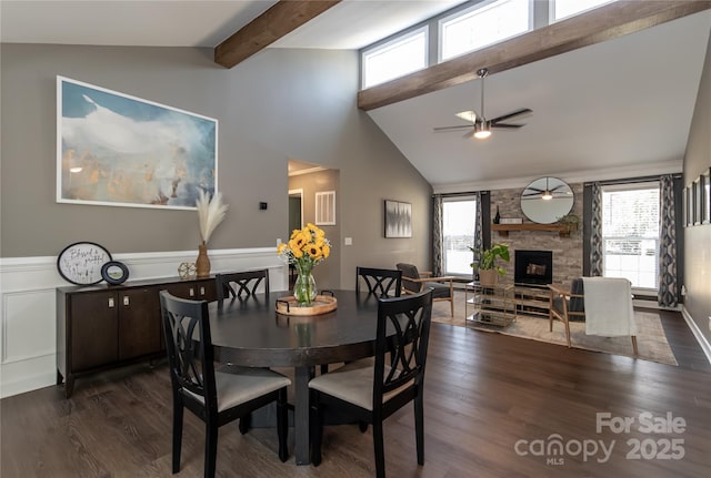 dining room with a wealth of natural light, a stone fireplace, beam ceiling, and dark wood-style floors