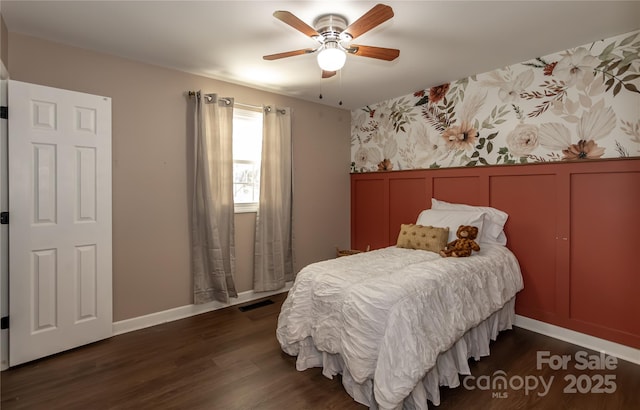 bedroom with visible vents, a ceiling fan, wainscoting, a decorative wall, and dark wood-style flooring