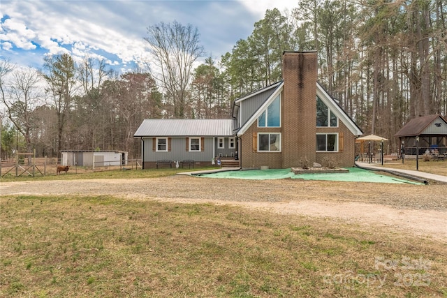 rear view of property featuring metal roof, brick siding, a lawn, and a chimney