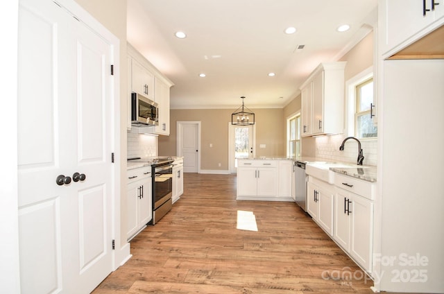 kitchen with light stone counters, light wood finished floors, stainless steel appliances, a sink, and a peninsula