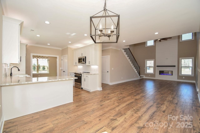 kitchen featuring a large fireplace, a sink, white cabinets, appliances with stainless steel finishes, and backsplash