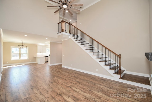 unfurnished living room with ceiling fan with notable chandelier, stairway, wood finished floors, and baseboards