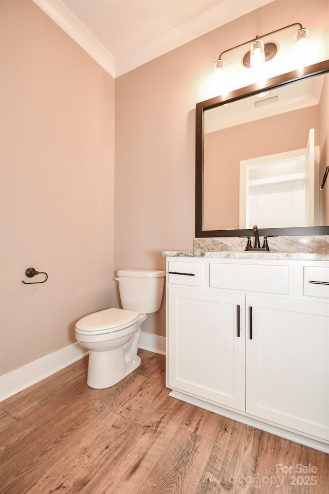 bathroom featuring toilet, wood finished floors, vanity, baseboards, and crown molding