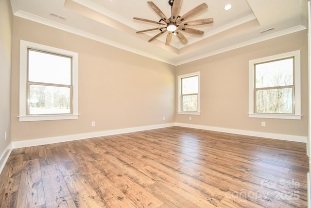 empty room featuring hardwood / wood-style flooring, a raised ceiling, visible vents, and crown molding