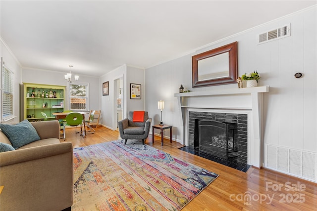 living area featuring ornamental molding, visible vents, a tiled fireplace, and wood finished floors